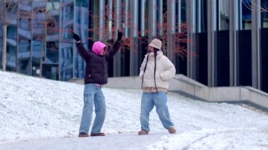 Sıcak kışlık palto giymiş iki kişi kalabalık bir şehirde karlı zeminde duruyor.