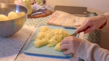 Bir kadın yetenekli bir şekilde mavi bir kesme tahtasının üzerinde taze patatesleri kesiyor ve yeteneğini sergiliyor.