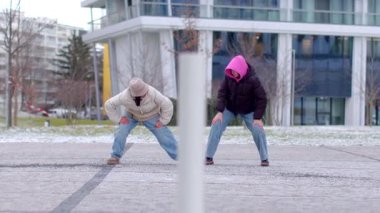 Kışlık giysiler içindeki iki birey, canlı bir şehir ortamında dışarıda neşe içinde etkileşime geçiyorlar.