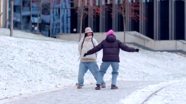 Ceket ve şapkalı iki kişi, modern bir binanın yanında kar üzerinde dikiliyorlar ve güzel bir manzara yaratıyorlar.