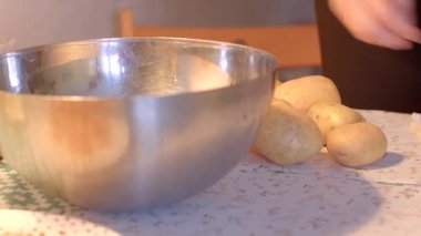 Masadaki patatesleri tutarken bir kase kullanarak çeşitli malzemeler hazırlayan bir kişi.