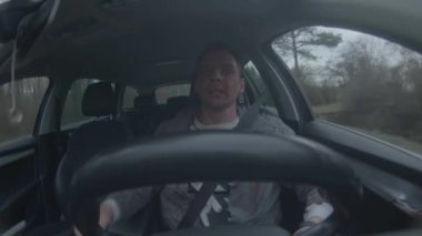 Sürücü, tamamen yemyeşil ağaçlarla çevrili bir yol boyunca giden bir aracın içinde oturuyor.