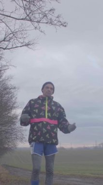 Canlı renkli bir ceket ve şort giyerken sisli bir arka planda enerjik bir şekilde koşan bir kişi.