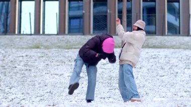 Bir çift, şehir manzarası tarafından çerçevelenmiş, yeni yağmış karda yürürken sevgi dolu bir şekilde el ele tutuşuyor.