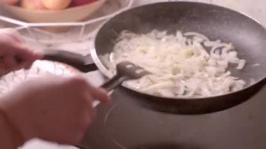 Bu videoda kızartma tavasında soğan pişiren bir kişi var, karıştırmak için çatal kullanıyor, karamelize ederken mutfak tekniklerini vurguluyor.