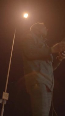 Bir birey, teçhizatını titizlikle, hareketli bir şehir gece sahnesinin arka planına göre düzenliyor.