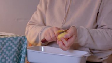 Bir birey, güzel desenli bir masada beyaz bir tabağın üzerine sarı bir limon soyuyor.