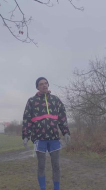 Kararlı bir koşucu sisli bir ortamda, renkli şort ve ceket giyer.