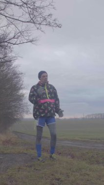 Canlı bir ceket giymiş bir koşucu ağaçlarla çevrili sisli ve sakin bir patika boyunca koşuyor.