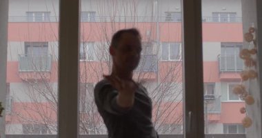 Huzurlu bir duruşu olan bir birey geniş bir pencerenin yanında oturur, yüksek gökdelenlere bakan bir şehir siluetine bakar.