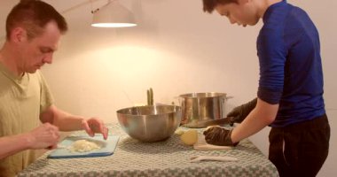 Mutfak tezgahında birlikte yemek pişiren iki insan takım çalışmasını ve becerilerini ön plana çıkarıyor.