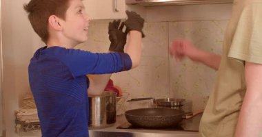 Küçük bir çocuk mutfaktaki ebeveyne mutluluk içinde yardım ederek aşçılık öğrenme deneyimlerini ön plana çıkarıyor.