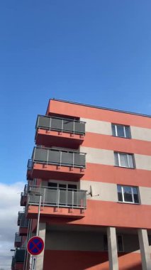 Şık, modern bir apartman dairesi gösteriliyor. Birden fazla balkon var. Parlak mavi gökyüzüne karşı güzelce dizilmiş.