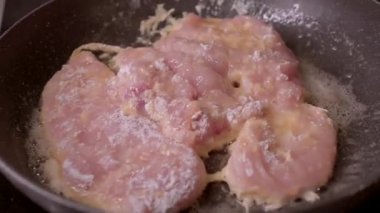 Bir tavuk göğsü tavada kızarıyor, güzel bir şekilde pişirme sürecini gösteriyor.