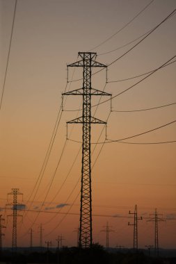Uzun bir sıra elektrik hattı, akşam güzelliğini yansıtan canlı renklerle dolu, nefes kesici bir günbatımına karşı siluet vaziyette duruyor.