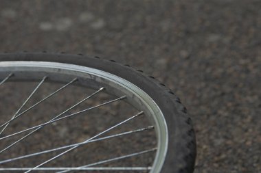 Bu görüntü, çakıllı bir yolda dinlenen bisiklet tekerleğinin ayrıntılı bir yakın çekimini, karmaşık tellerini ve lastik yüzeyinin dokusunu gösteriyor.