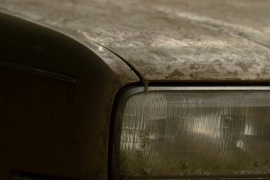 Görüntü, kirli bir arabanın kaputunun ve farının yakın plan görüntüsünü sunuyor. Zamanla biriken aşınma ve kiri ortaya çıkarıyor.