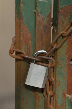 Sağlam bir asma kilit, uzun paslı bir zincire sıkı sıkıya bağlıdır. Güvenlik hissi verir ama aynı zamanda yaş ve aşınma belirtileri de gösterir.