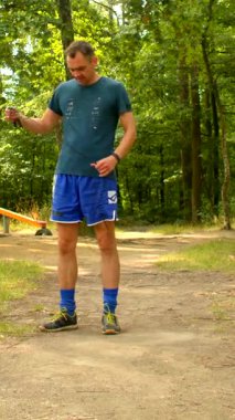 Bir adam dingin ormanlık ve park ortamlarında spor yapıyor, şınav çekiyor ve ayakkabılarını bağlıyor, sağlığı doğayla dengeliyor.