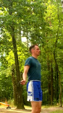 Canlı şortlu bir adam ormanda bir gün geçirmekten zevk alır, telefonunu kontrol eder, dürbünle gözlemler, frizbi atar, esner ve koşar.