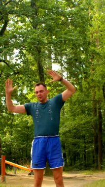 Huzurlu bir parkta, yeşil ve mavi elbiseli bir adam esner ve egzersiz yapar, somut odak ve kararlılık, açık hava fitness ilham verici