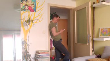 Sıcak bir oturma odasında, bir kadın telefonuyla konuşurken bir erkek duvara yaslanıp telefonuna odaklanıyor. Sahne bağlantıyı ve dikkat dağınıklığını gösterir