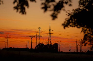 Ön planda belirgin elektrik hatları bulunan nefes kesici bir günbatımı. Arka planda güzel ağaçlar zarif bir şekilde konumlanmış.