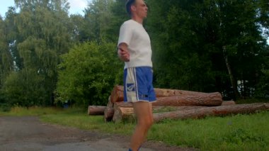 Canlı bir park sahnesinde beyaz gömlekli ve mavi şortlu bir adam neşe içinde ip atlıyor, koşuyor, koşuyor ve açık havada egzersiz yapıyor.