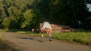 Bir adam kaykay yeteneklerini manzaralı bir parkta sergiliyor, eğlenceli manevraları harmanlıyor, doğa yansıması, koşu ve heyecan verici bir amuda kalkıyor.