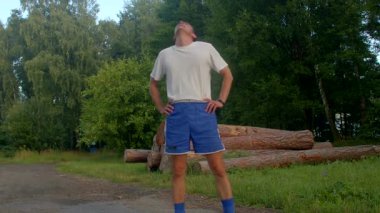 Bu canlı videoda beyaz tişörtlü ve mavi şortlu bir adam parkta çeşitli aktiviteler yapıyor, neşe ve uygunluğu ifade ediyor.