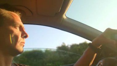 Otoyolda araba kullanan bir adam, hoşnutsuzluk ve iç gözlem gibi duyguları dışa vurarak pencereden dışarıyı seyrediyor.