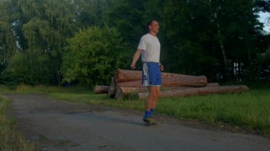 Bir adam toprak bir yolda, doğa güzelliğinin ortasında ip atlama egzersizi yapıyor. Video, doğadaki zindeliği vurgulayarak huzurlu bir park ve ormana karşı ritmik sıçramalarını gösteriyor.