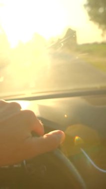 Güneşli bir günde, bir insan kendinden emin bir şekilde araba kullanır, güneş ışığı ön camdan akar, eller direksiyonda, özgürlük ve macerayı somutlaştırır.