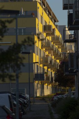 Parlak, neşeli, sarı bir apartman binası. Şehir planına ve tasarıma cazibe ve tarz katan sayısız balkon barındırıyor.