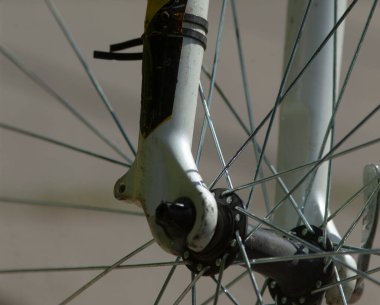 Bu görüntü, bir bisiklet tekerleğinin detaylı bir yakın görüntüsünü sağlar, tekerleğin karmaşıklığını ve ona sıkıca bağlı bir çatalı gösterir.