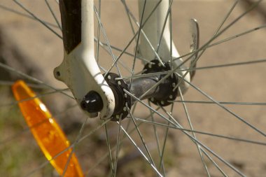 Bu görüntü, tekerlek bileşenlerini vurgulayan parlak turuncu bir yansıtıcının yer aldığı bisiklet tekerleğinin detaylı bir yakın görüntüsünü sunar.