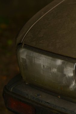 Burada çok kirli bir arabanın kaputu ve farının detaylı bir yakın çekimi var, kusurları ve otomotiv bakımının ihmalkarlığını vurguluyor.