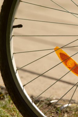 Bisiklet sürme faaliyetleri sırasında görünürlüğü ve güvenliği arttıran turuncu bir yansıtıcının yer aldığı bir bisiklet tekerleğinin ayrıntılı yakın çekim görüntüsü