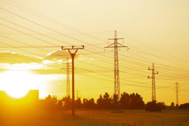 Resimli bir sahnede, günbatımının renkleriyle güzelce aydınlatılmış, geniş bir açık alan boyunca uzanan uzun bir kablo hattı var.