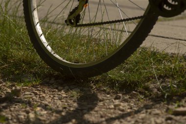 Bu görüntü, engebeli çakıllı bir yolda dinlenen bir bisiklet tekerleğinin detaylı bir yakın görüntüsünü içeriyor.