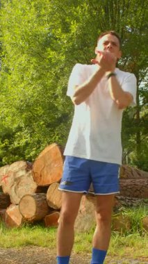 Beyaz tişörtlü bir adam ve şık mavi şortlu bir adam büyük bir kütük yığınının önünde güvenle duruyor.