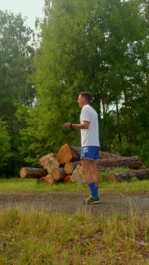 Sıradan giyinmiş bir adam toprak bir yol boyunca yürür ve koşar. Büyük bir odun yığınının arasından. Açık hava macerası ve doğal huzuru yakalar.