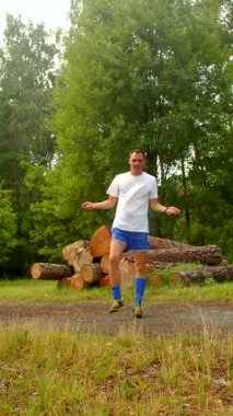 Huzurlu bir ormanda, bir adam bir kütük yığını tarafından enerjik bir şekilde ip atlıyor, sakin bir arka plana karşı azim ve güç sergiliyor.