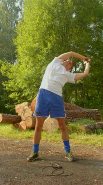 Huzurlu bir ormanda, bir adam sağlık konusundaki bağlılığını esneme ve amuda kalkma gibi etkinliklerle gösterir.