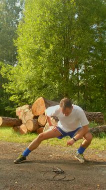 Günlük giysiler içindeki bir adam, bir yığın kütüğün yanında uzanıyor, sakin açık hava ortamının tadını çıkarıyor ve doğa ile refah arasındaki bağlantıyı vurguluyor.