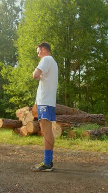 Bu videoda, bir adam dingin bir ormanlık alanda çeşitli fiziksel aktiviteler sergiliyor. Kütüklerin üzerine eğiliyor, yol kenarında geriniyor, ve ip atlıyor, neşeli ve aktif bir yaşam tarzını somutlaştırıyor.