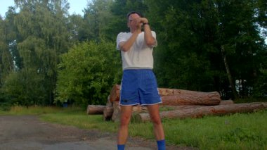 Bu videoda, beyaz gömlek ve mavi şort giymiş, güç ve denge sergileyen bir adam parkta etkileyici amuda kalkma becerileri sergiliyor.