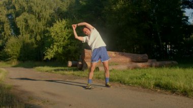 Bu video, doğayı kucaklayan, esneyen ve ağaçlık bir yolda dans eden bir adamı gösteriyor. Neşeli ruhu refahı ve dışarıdaki zevkleri arttırır.