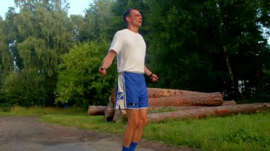 Bu videoda, beyaz gömlekli ve mavi şortlu bir adam spor ve çevikliğe olan bağlılığını sergileyerek manzaralı bir parkta koşuyor.