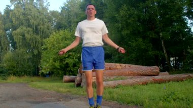 Beyaz tişörtlü ve mavi şortlu bir adam canlı bir parkta ip atlıyor, açık hava fitness somutlaştırıcı ve etkin bir yaşam tarzı